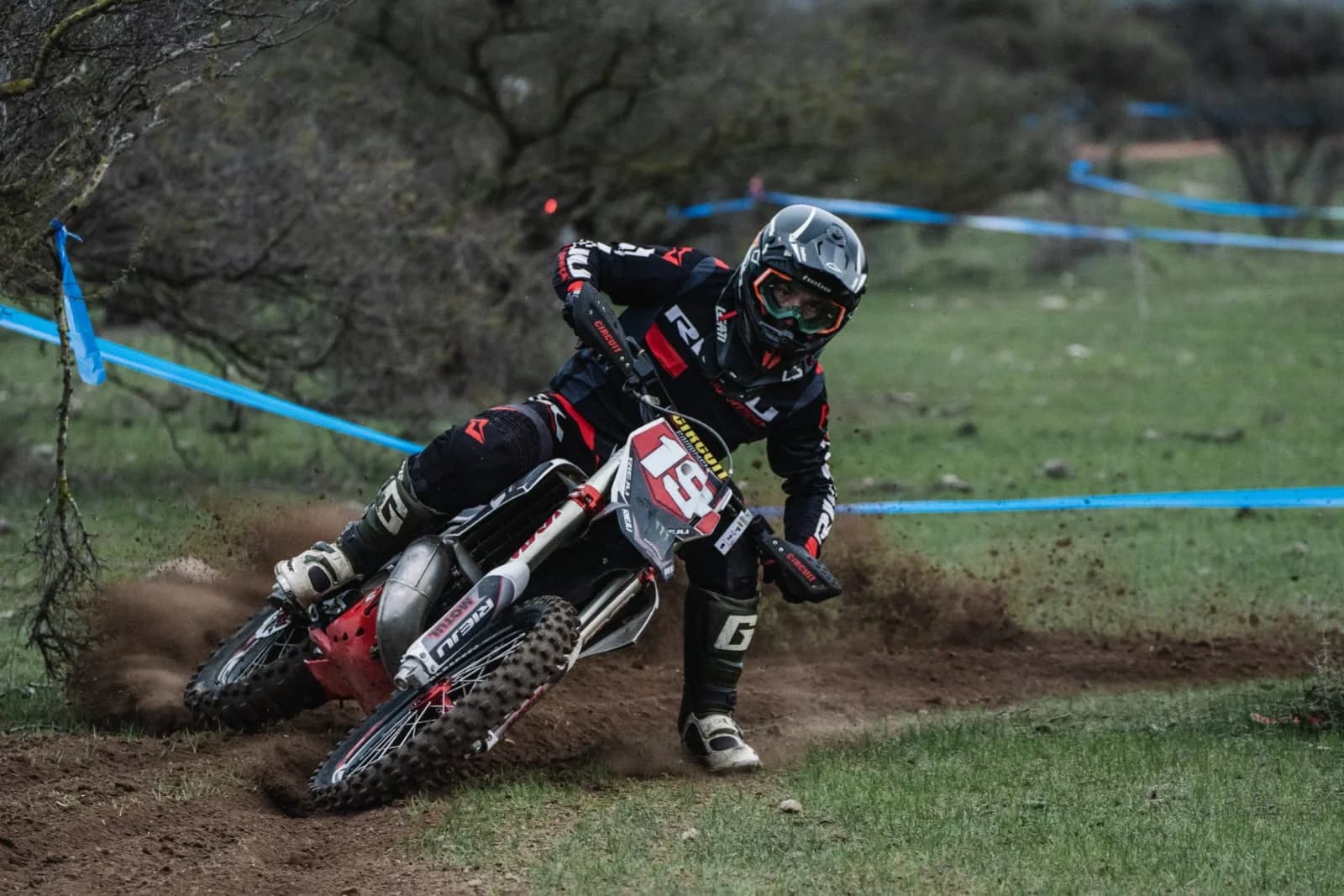 Piloto del equipo Proride inclinando la moto de enduro en una curva de tierra, levantando polvo, durante una carrera